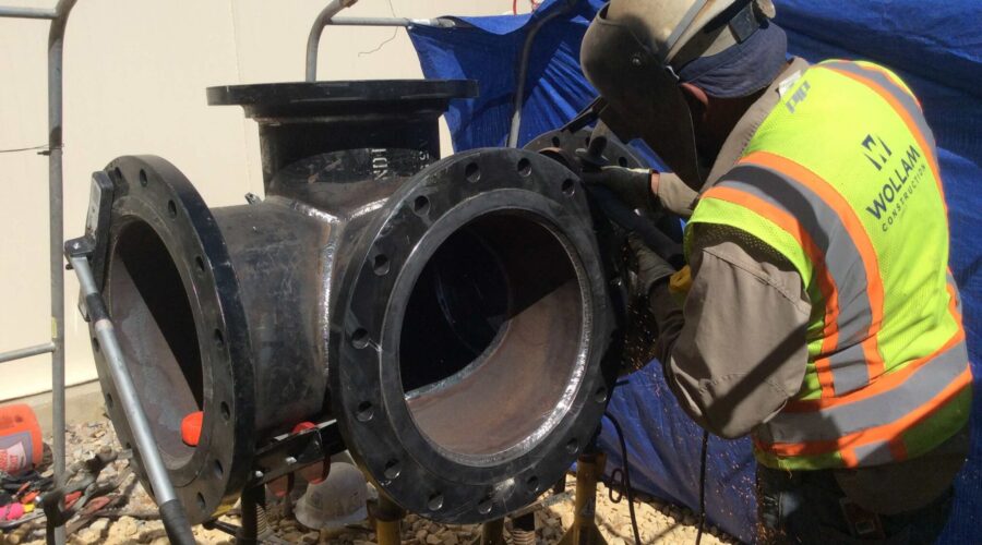 Welder Grinding Metal Pipe Joint for Underground Piping Installation | Wollam Construction